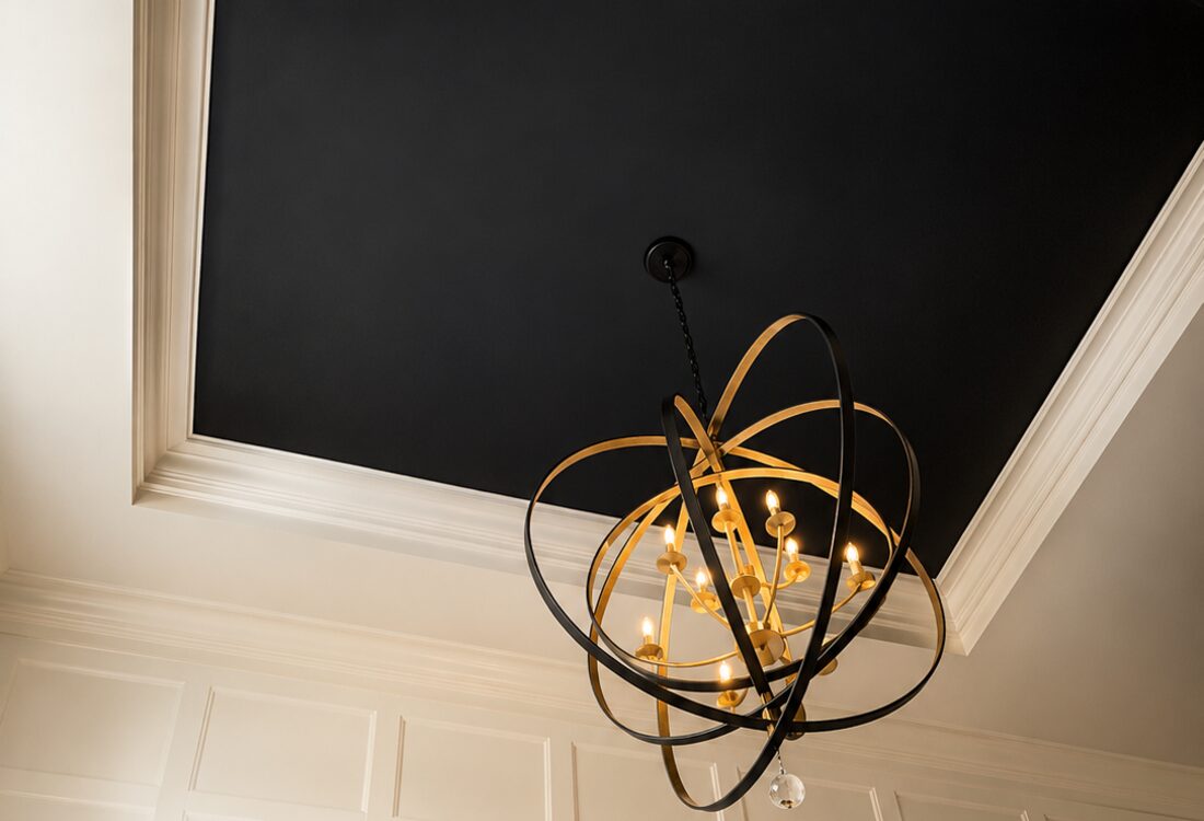 Black tray ceiling with a brass-and-bronze orb chandelier above white paneled walls.